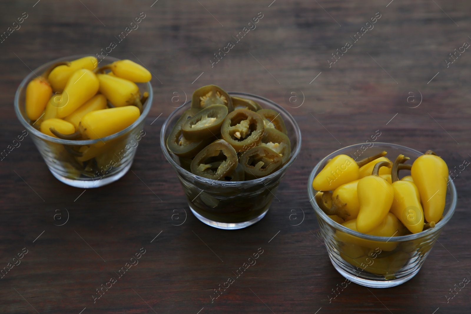 Photo of Pickled green and yellow jalapeno peppers on wooden table