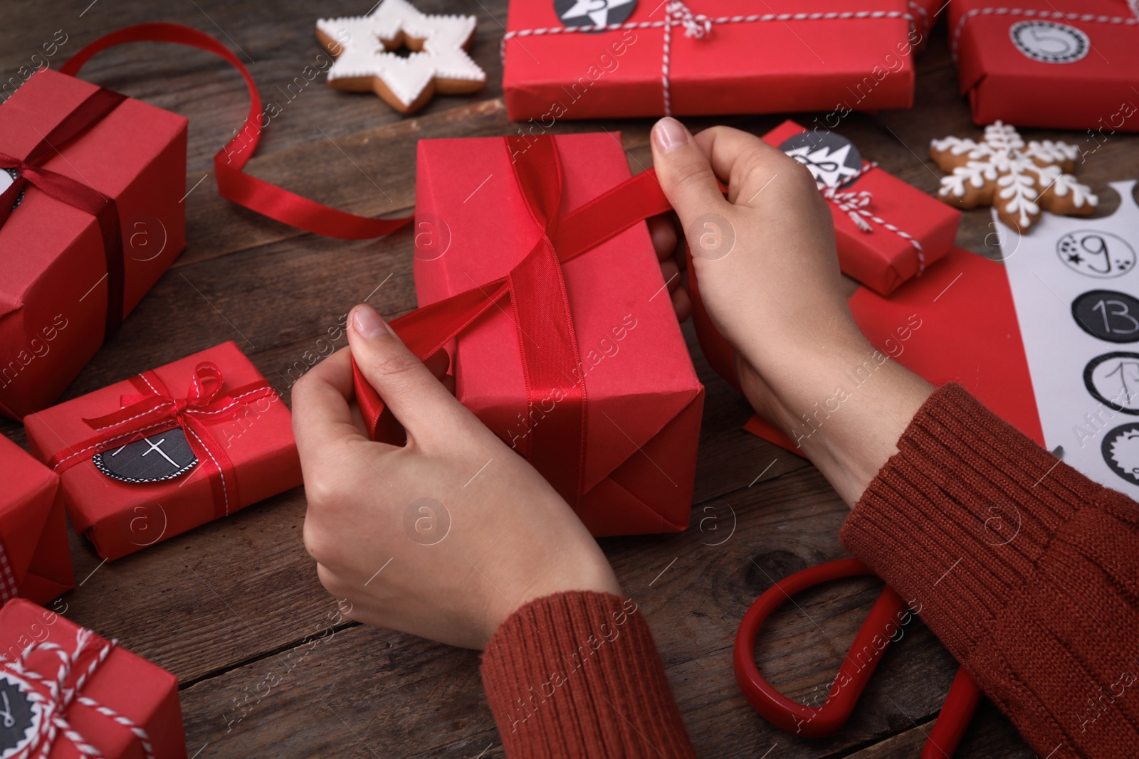 Photo of Woman decorating gift box at wooden table, closeup. Creating advent calendar