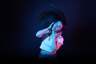 Photo of Happy woman in headphones listening music and dancing in neon lights against dark blue background
