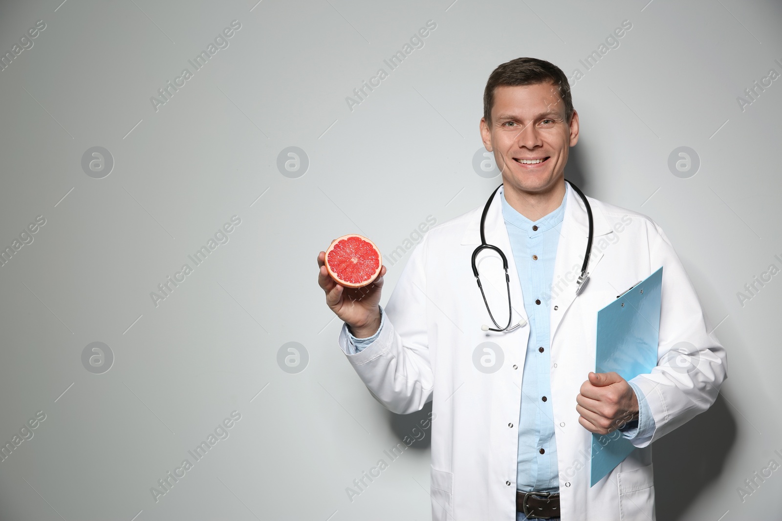 Photo of Nutritionist with ripe grapefruit and clipboard on light grey background. Space for text