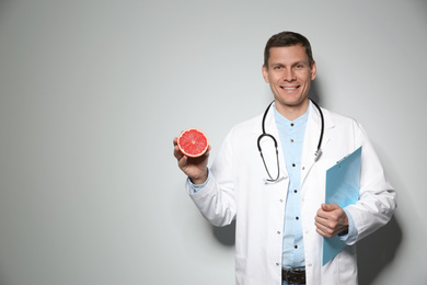 Photo of Nutritionist with ripe grapefruit and clipboard on light grey background. Space for text