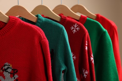 Photo of Different Christmas sweaters hanging on rack against beige background, closeup