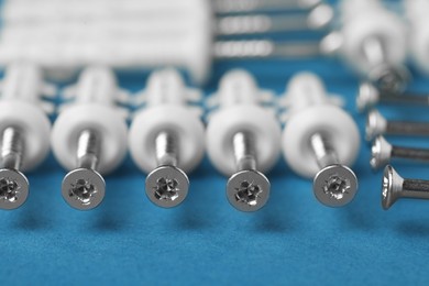 Photo of Many metal screws with white dowels on blue background, closeup