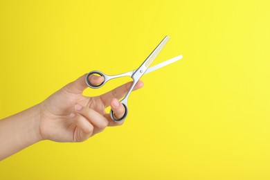 Hairdresser holding professional thinning scissors on yellow background, closeup. Haircut tool