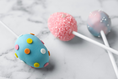 Photo of Egg shaped cake pops for Easter celebration on white marble table, closeup