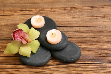 Pile of spa stones with lit candles and flower on wooden background, space for text