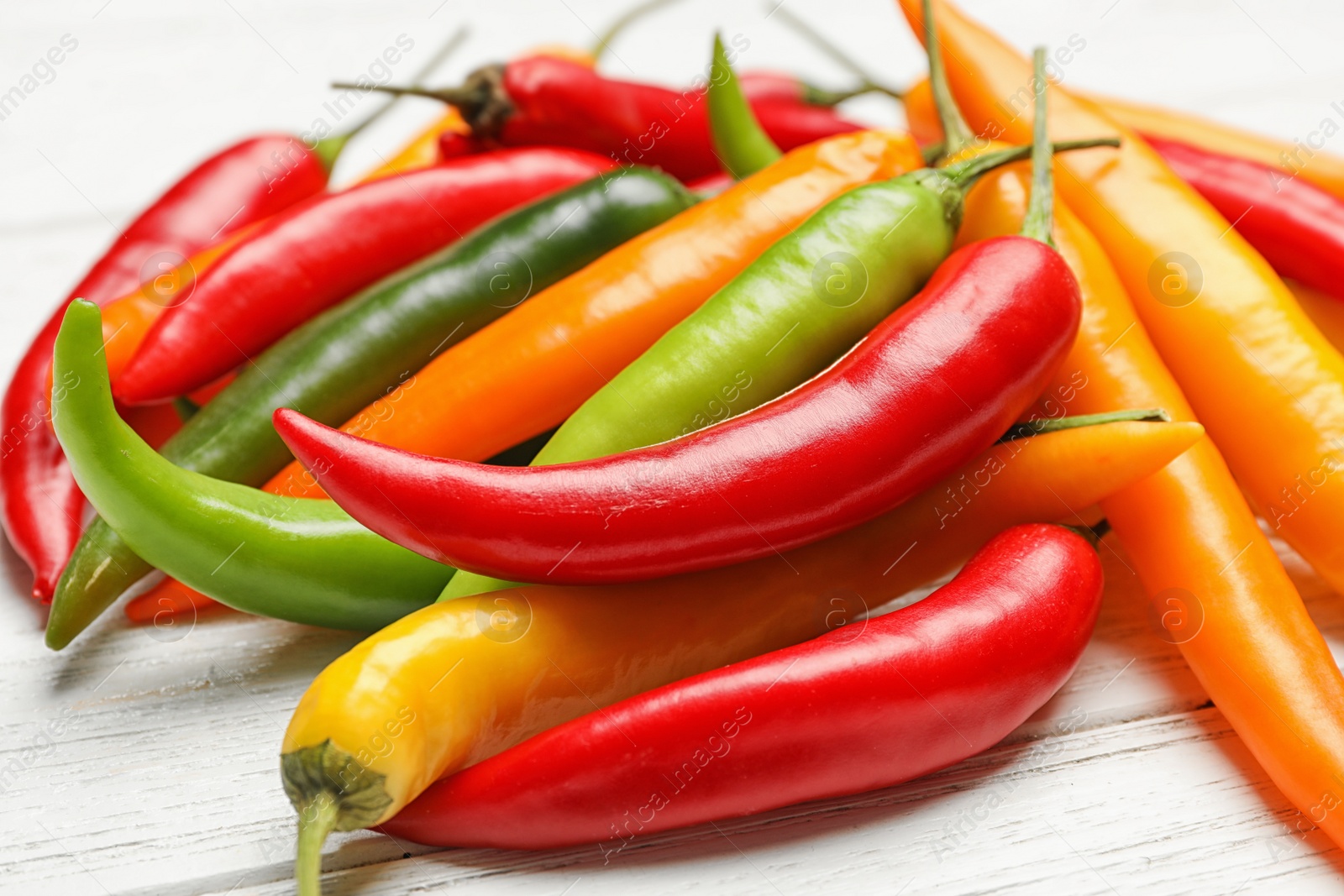 Photo of Different hot chili peppers on white wooden table, closeup