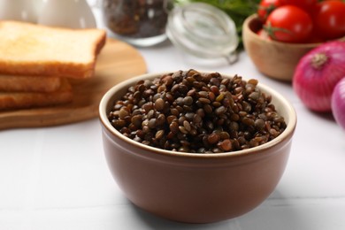 Photo of Delicious lentils in bowl served on white table, closeup
