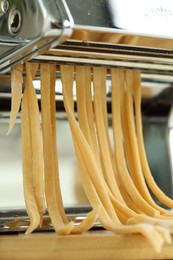 Pasta maker with raw dough on wooden table, closeup