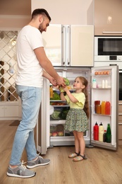 Photo of Young father and daughter with broccoli near refrigerator at home