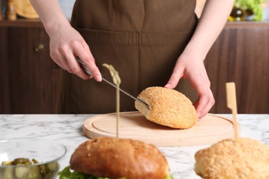 Photo of Woman making delicious vegetarian burger at white marble table, closeup