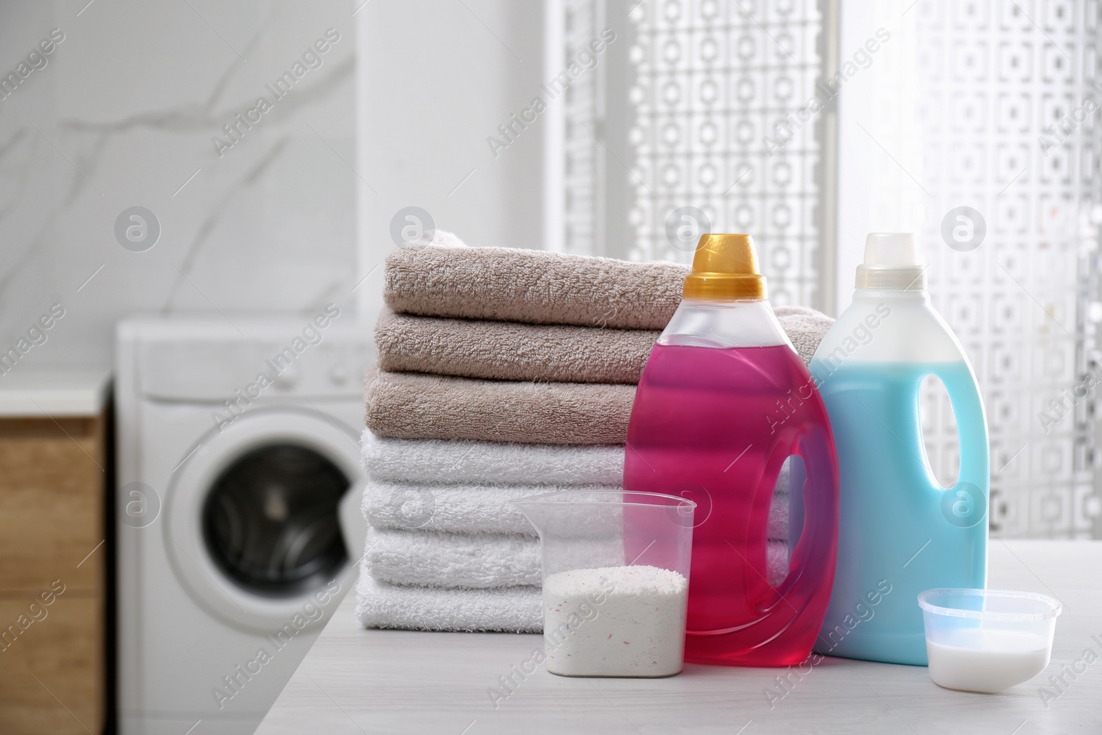 Photo of Stack of folded towels and detergents on white table in bathroom