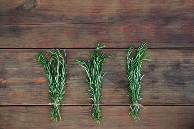 Photo of Bunches of fresh rosemary on wooden table, flat lay. Aromatic herb