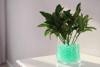 Photo of Mint filler with green branches in glass vase on white table, space for text. Water beads