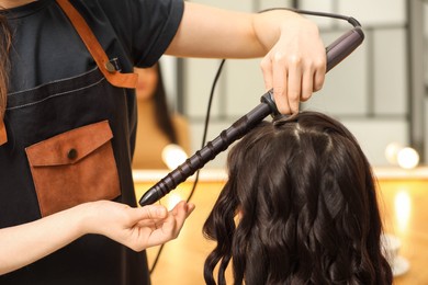 Photo of Hair styling. Hairdresser curling woman's hair in salon, closeup