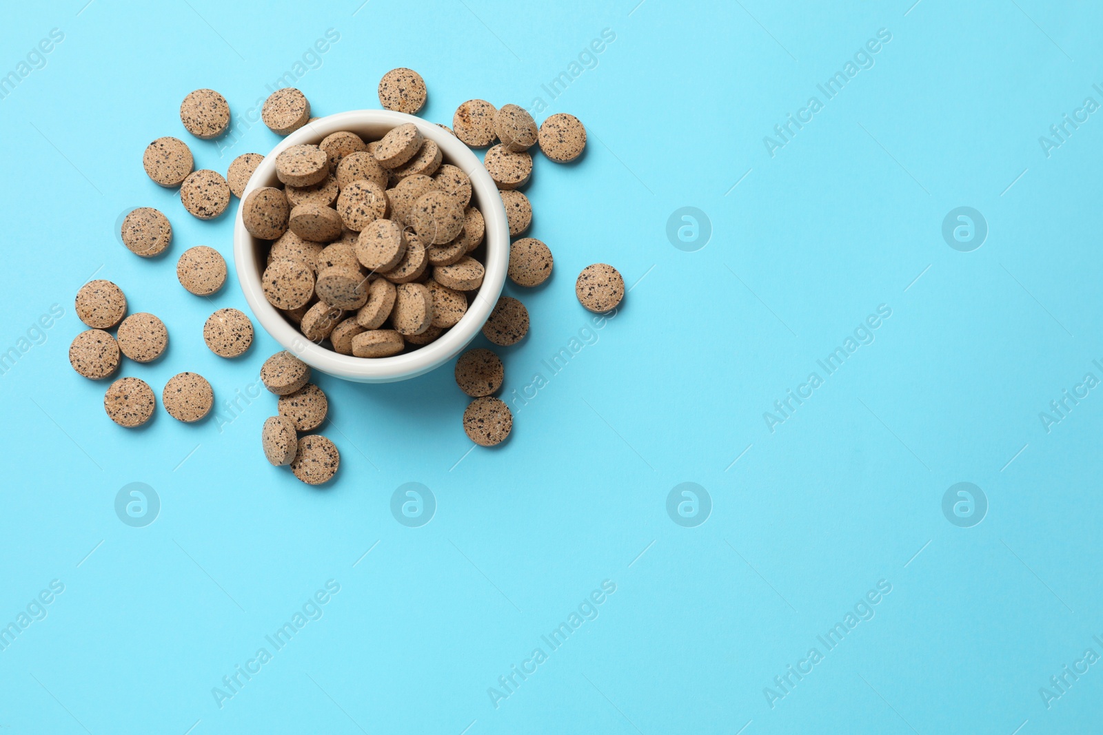 Photo of Vitamin pills in bowl on light blue background, top view. Space for text