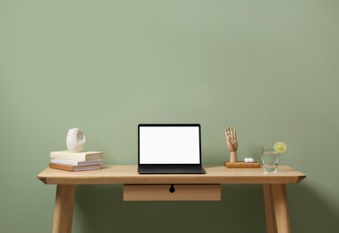 Photo of Stylish workplace with laptop, books and decor on table near light green wall