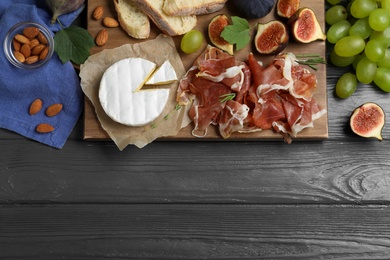 Board with delicious figs, proscuitto, cheese and grapes on grey wooden table, flat lay. Space for text