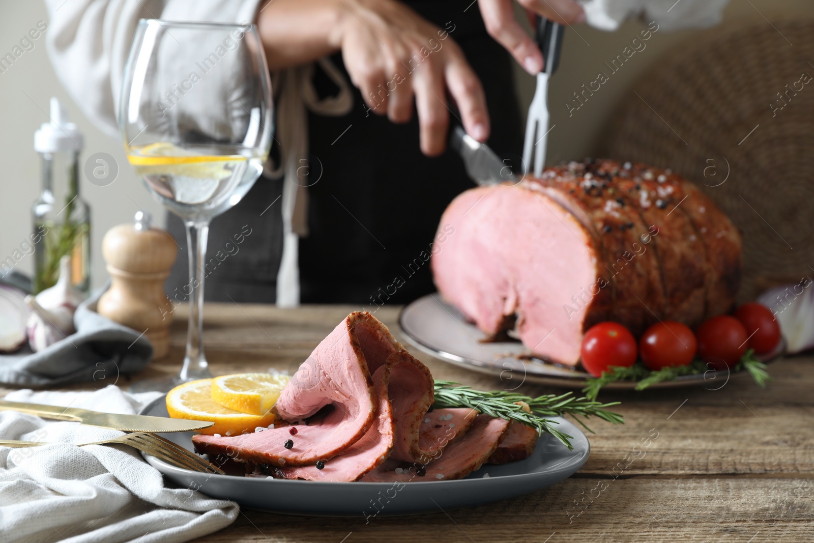 Photo of Woman cutting delicious baked ham at wooden table, selective focus