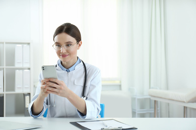 Photo of Young female doctor with smartphone at table in office