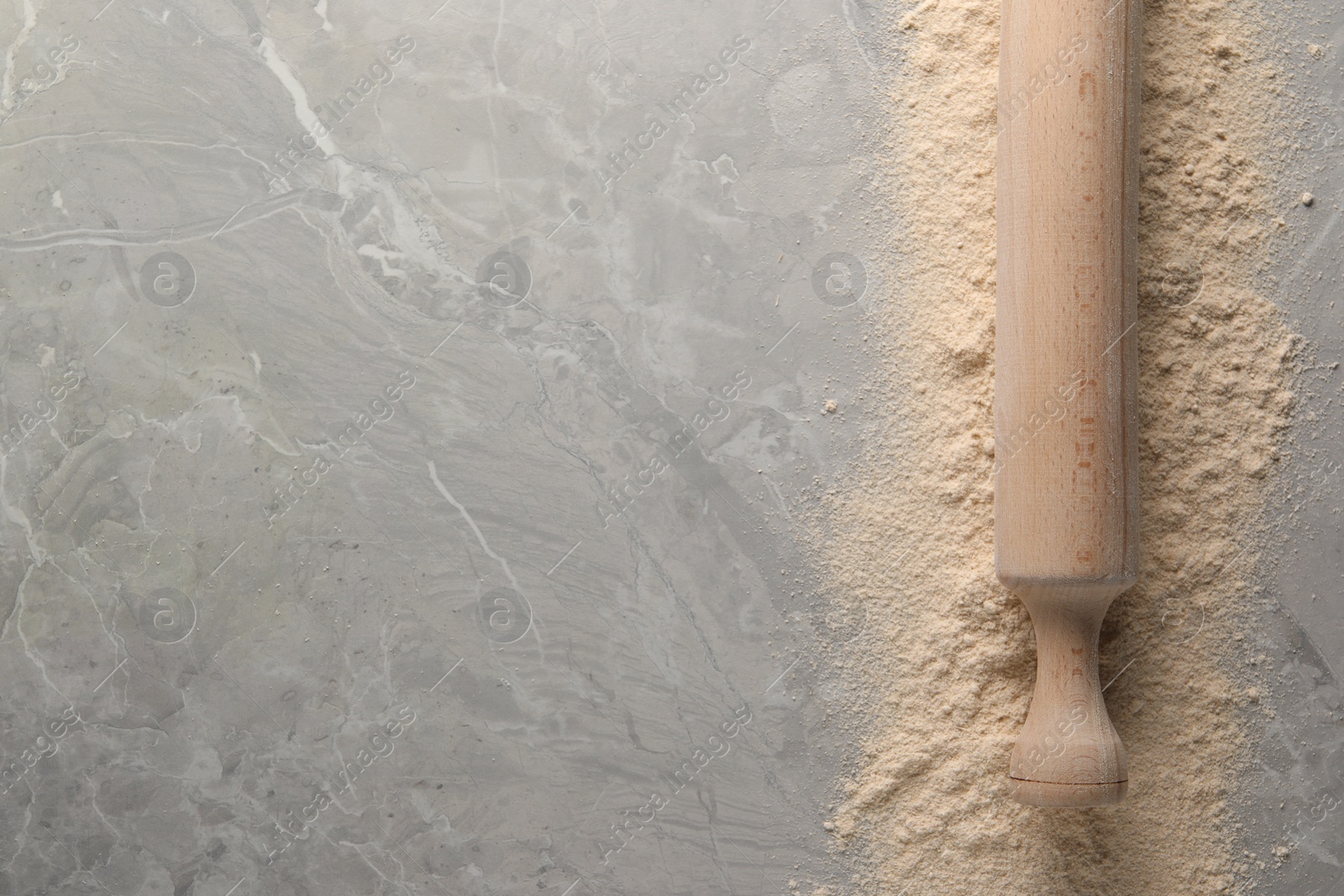 Photo of Flour and rolling pin on grey marble table, top view. Space for text