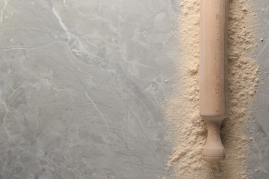 Flour and rolling pin on grey marble table, top view. Space for text