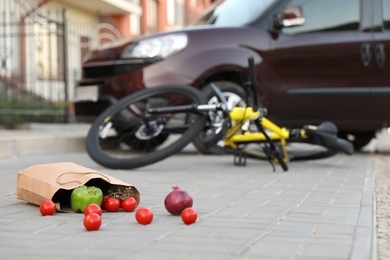 Photo of Fallen bicycle after car accident outdoors, focus on scattered vegetables