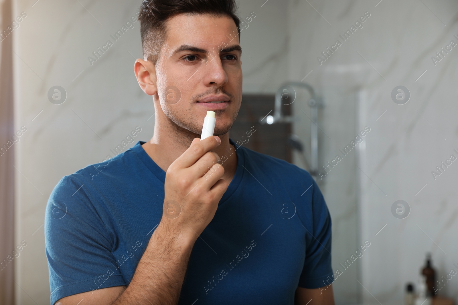 Photo of Man applying hygienic lip balm in bathroom