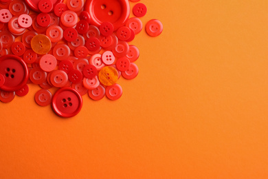 Many red sewing buttons on orange background, flat lay. Space for text