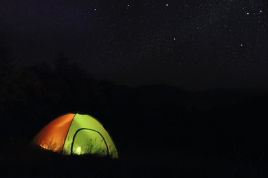 Photo of Camping tent glowing at night outdoors. Space for text