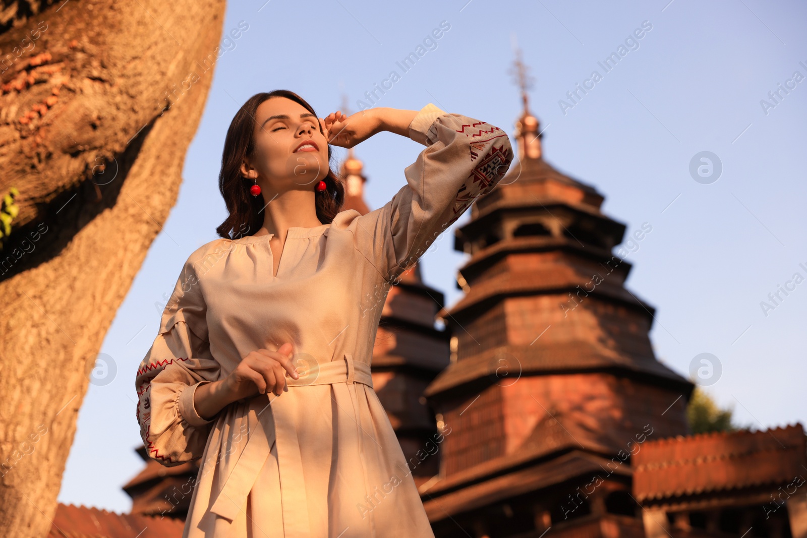 Photo of Beautiful woman wearing embroidered dress near old wooden church in village. Ukrainian national clothes