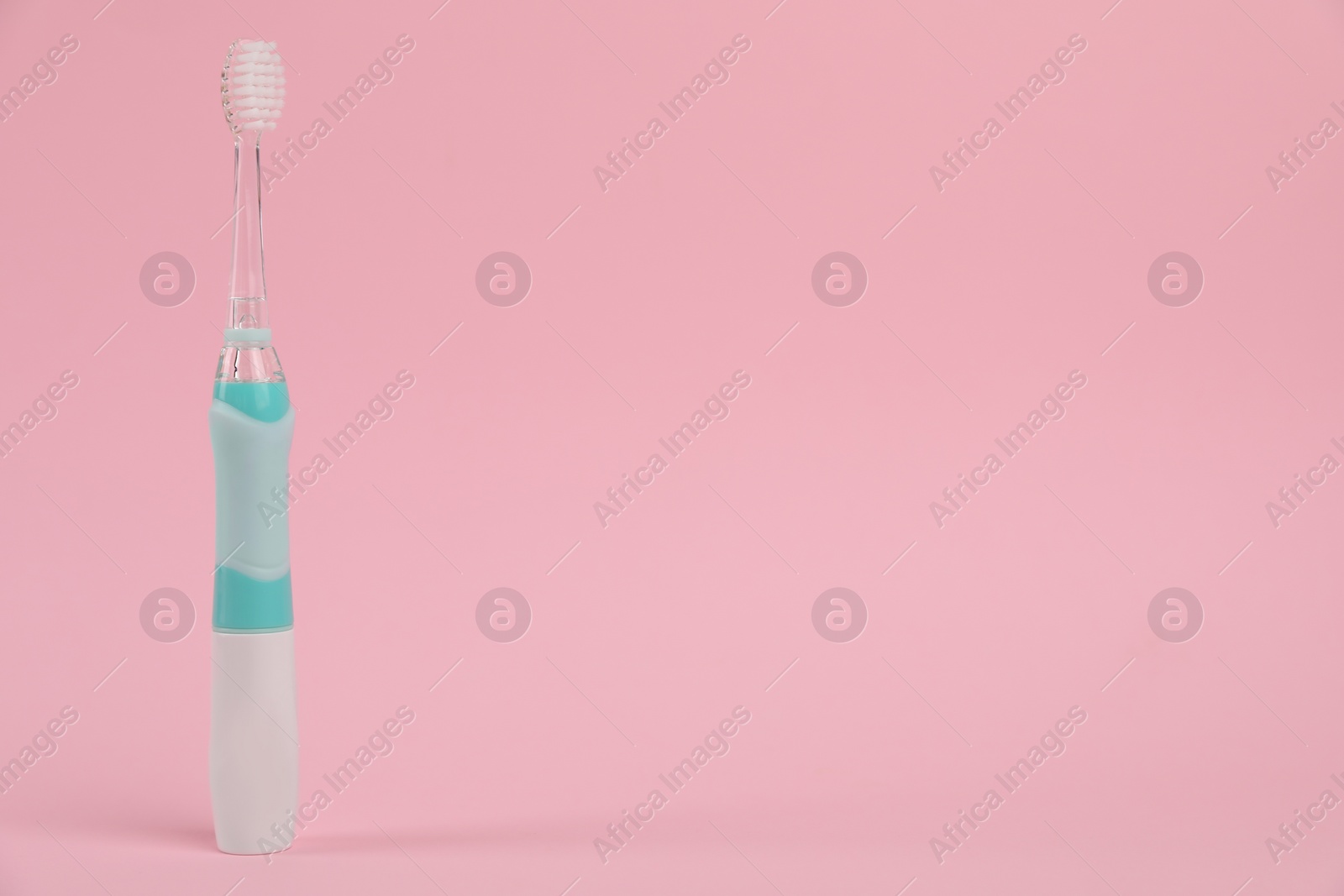 Photo of Electric toothbrush on pink background, space for text