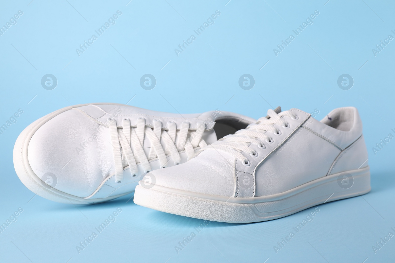 Photo of Pair of stylish white sneakers on light blue background