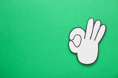 Paper cutout of okay hand gesture on green background, top view. Space for text