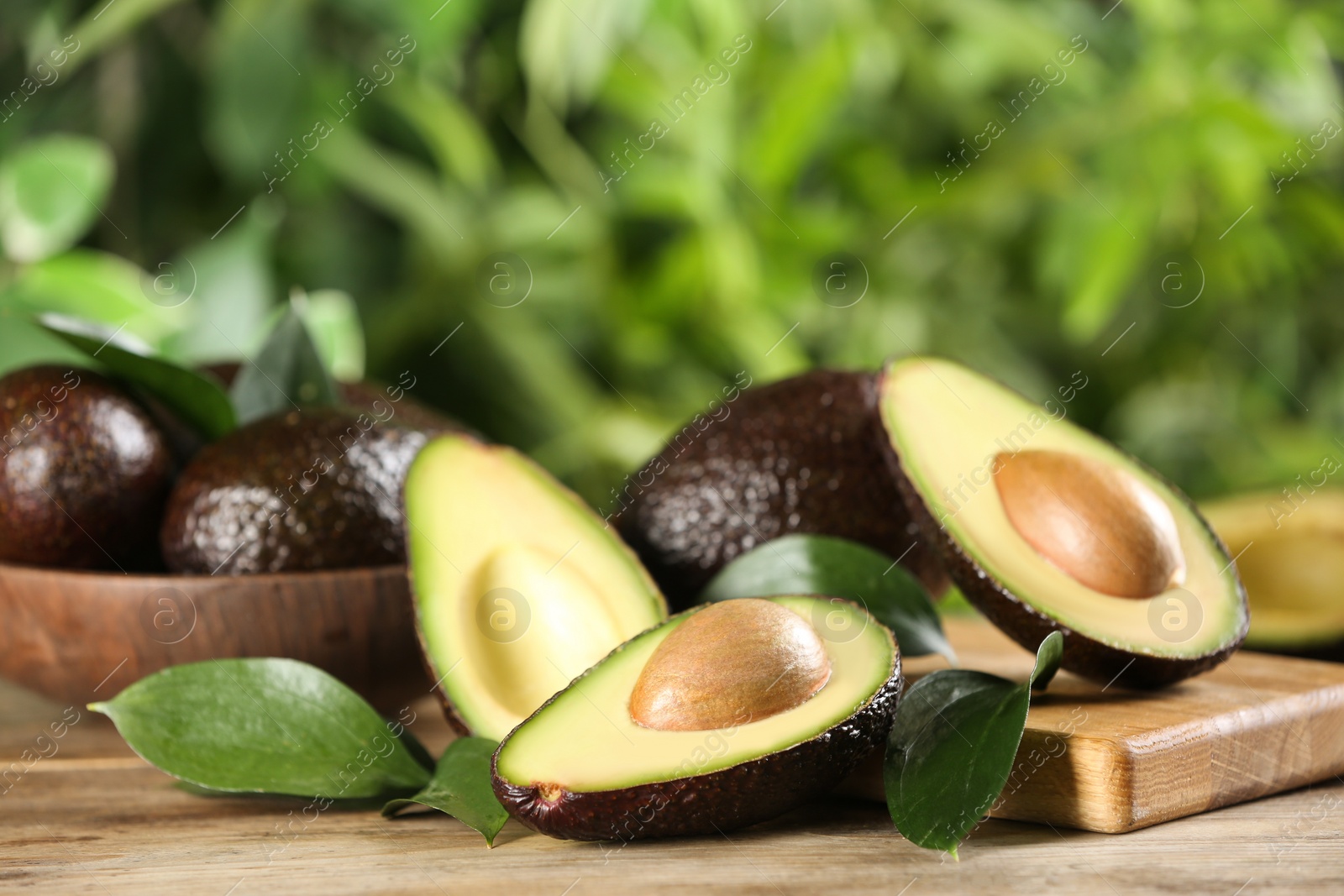 Photo of Whole and cut avocados with green leaves on wooden table