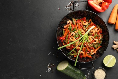 Photo of Shrimp stir fry with vegetables in wok and ingredients on black table, flat lay. Space for text