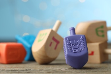 Photo of Hanukkah celebration. Dreidels with jewish letters on wooden table against light blue background with blurred lights, closeup