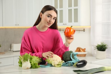 Woman taking vegetables out from string bag at light marble table in kitchen