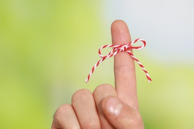 Man showing index finger with tied bow as reminder on green blurred background, closeup