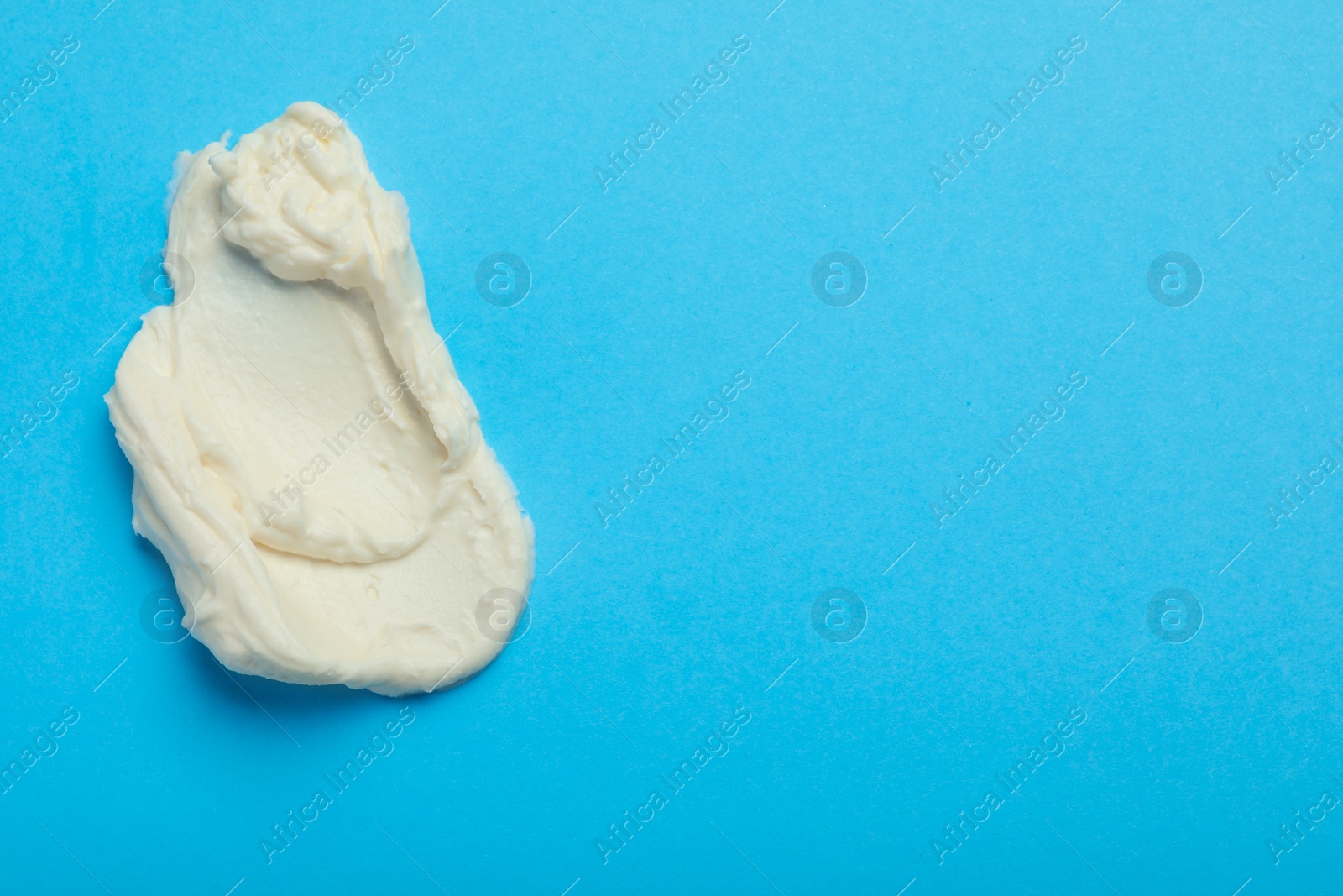 Photo of Smear of delicious cream cheese on light blue background, top view. Space for text