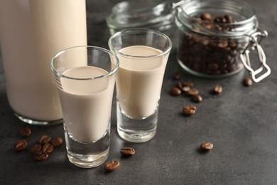 Photo of Coffee cream liqueur in glasses, bottle and beans on grey table, closeup