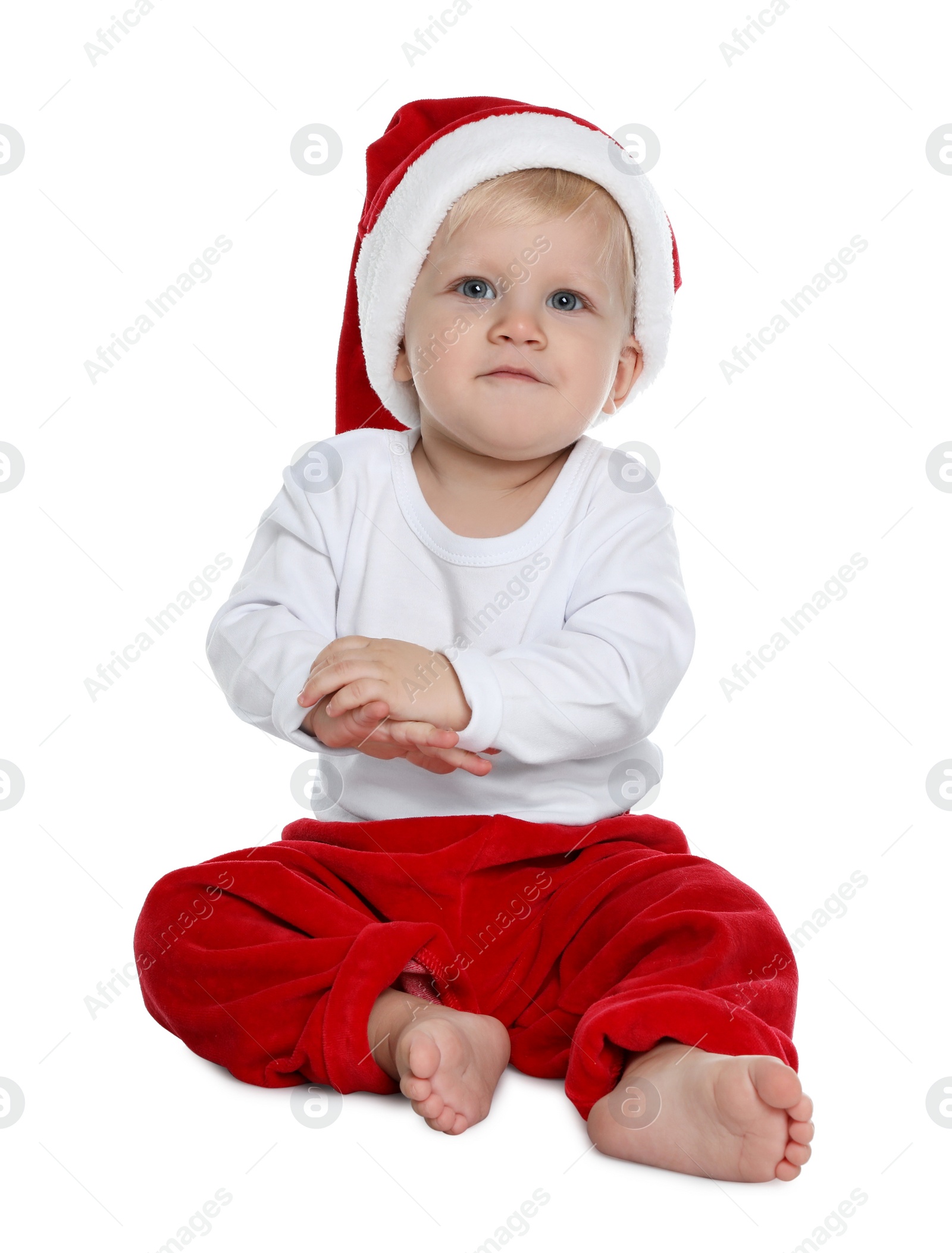 Photo of Cute baby in Santa hat and Christmas pajamas sitting on white background