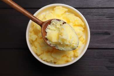 Photo of Bowl and spoon of Ghee butter on wooden table, top view