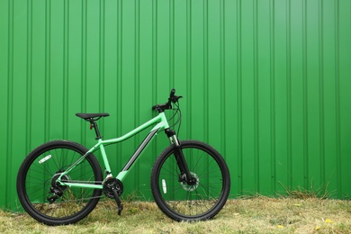Photo of Modern bicycle near green metal fence outdoors. Space for text