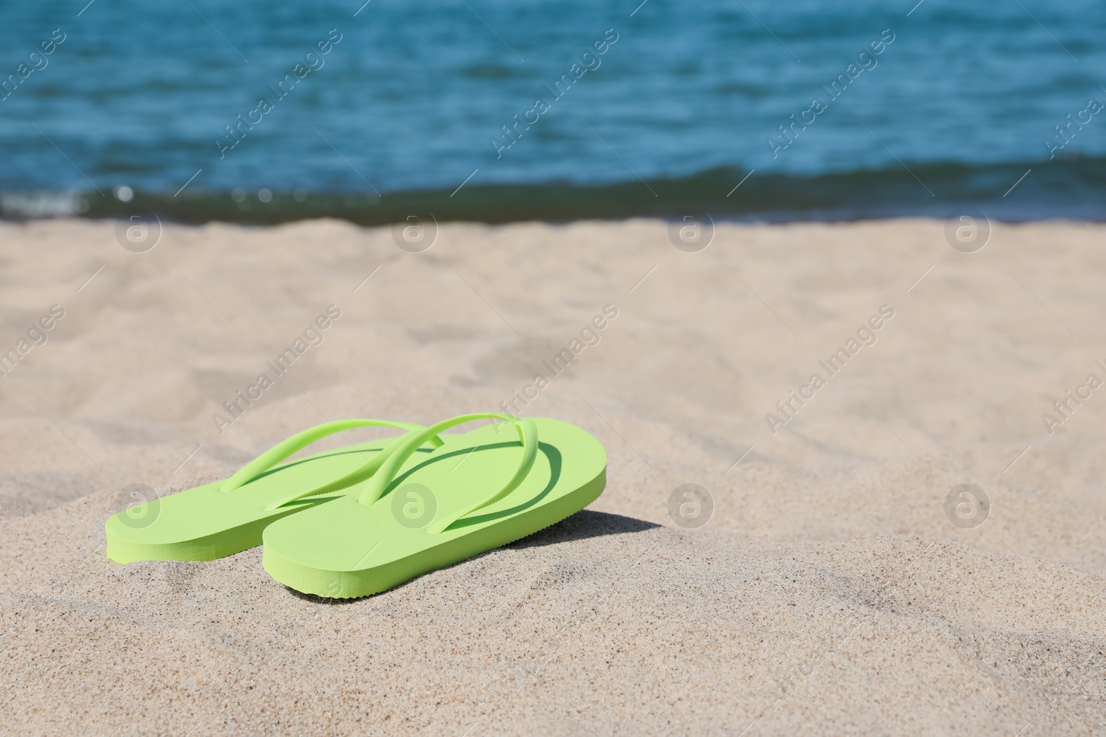 Photo of Stylish light green flip flops on beach sand, space for text