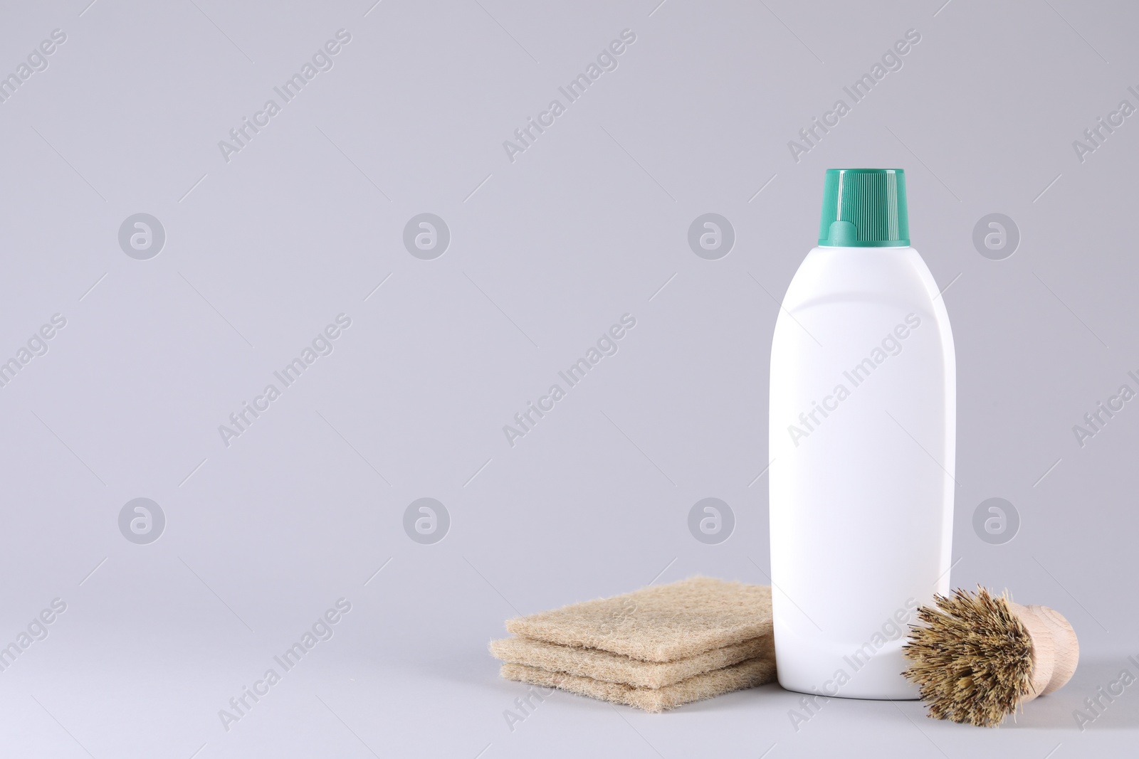 Photo of Bottle of cleaning product, brush and sponges on light background. Space for text