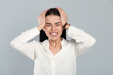 Woman suffering from migraine on grey background