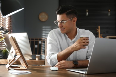 Photo of Freelancer with cup of coffee working at table indoors