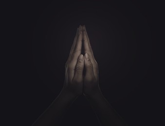 Image of Christian woman praying in darkness, closeup. Belief