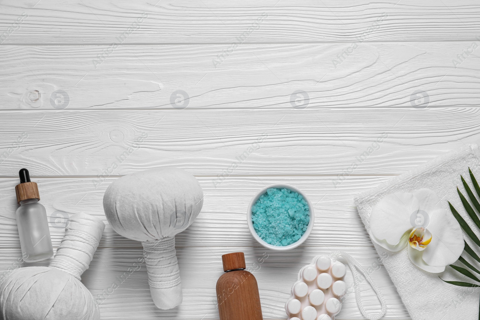 Photo of Beautiful spa composition with herbal massage bags and different care products on white wooden table, flat lay. Space for text